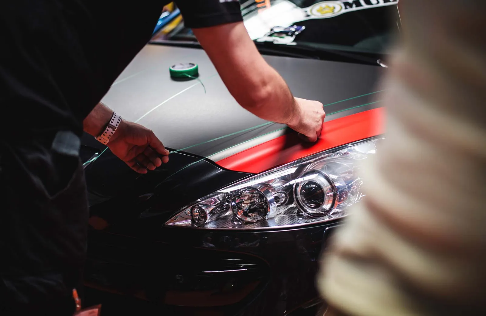 Car wrapping, man cuts protective foil or film. Car wrapping, man cuts protective vinyl foil or film on vehicle hood closeup. Worker makes auto detailing. Automobile paint protection coating, professional tuning